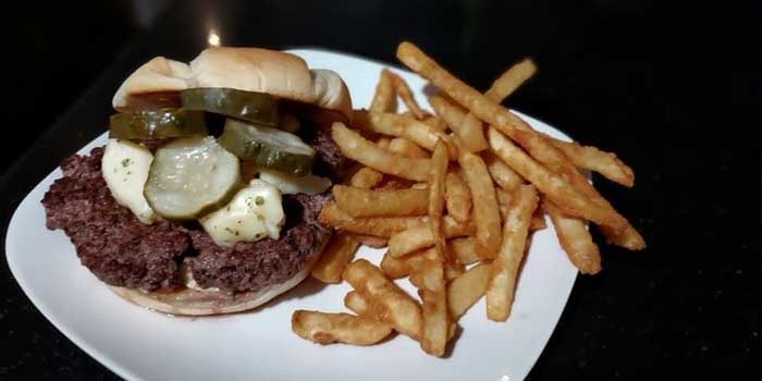 Delicious hand crafted burger topped with pickles and served with fries at The Flagstone in Appleton WI.